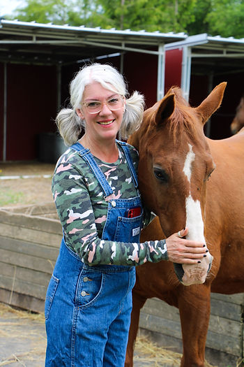 Woman holding horse head next to horse shelter