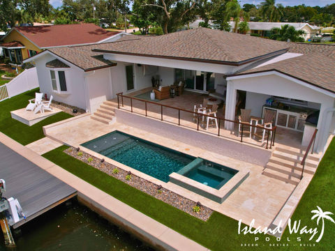 Linear, Waterfront Pool Featuring A Spillover Spa, Sunshelf, Outdoor Kitchen, Travertine Decking, & Artficial Turf