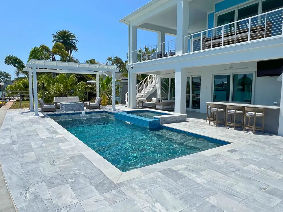 Modern, waterfront home with a linear pool, patio bar, spillover spa, and fire table under a pergola. Surrounded by palm trees and Italian marble decking.