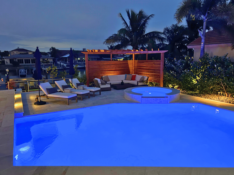 Pool, spillover spa, and pergola at night with lighting