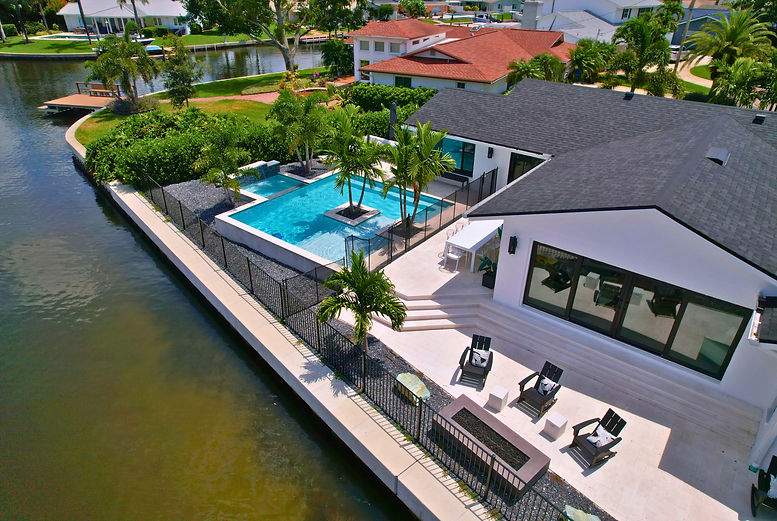 Drone Shot Of A Modern Outdoor Living Space Featuring A Geometric Pool, Flush Spa, Cascading Water Feature, Custom Planters, and Shellock Decking In Pinellas County