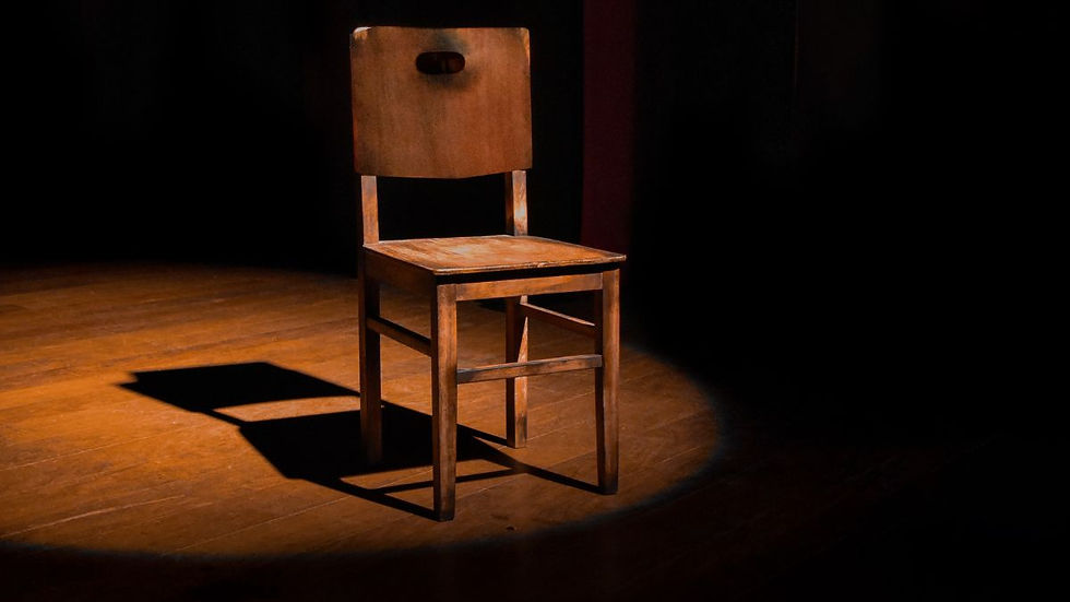 Empty wooden chair illuminated by spotlight on dark stage, symbolizing absence and loss on Father's Day