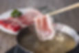 A hot pot with thin slices of meat ready to be dipped and cooked in boiling broth.