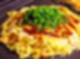 A layered Hiroshima-style okonomiyaki with noodles, cabbage, and various toppings.