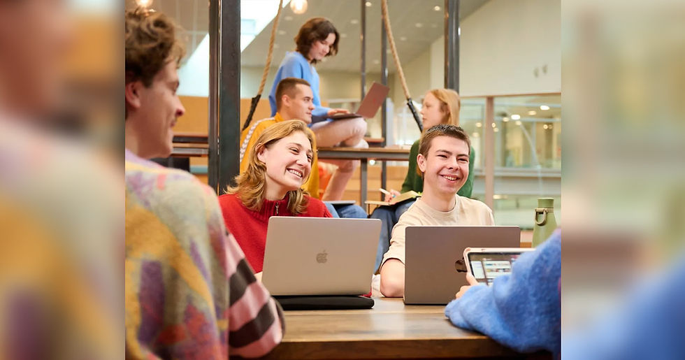 Group of students smiling, working on laptops in a bright, modern library. Warm colors, casual outfits create a relaxed, collaborative mood.