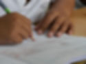 Gros plan sur les mains d’un enfant écrivant dans un cahier quadrillé avec un crayon de bois, travaillant sur un exercice scolaire.
