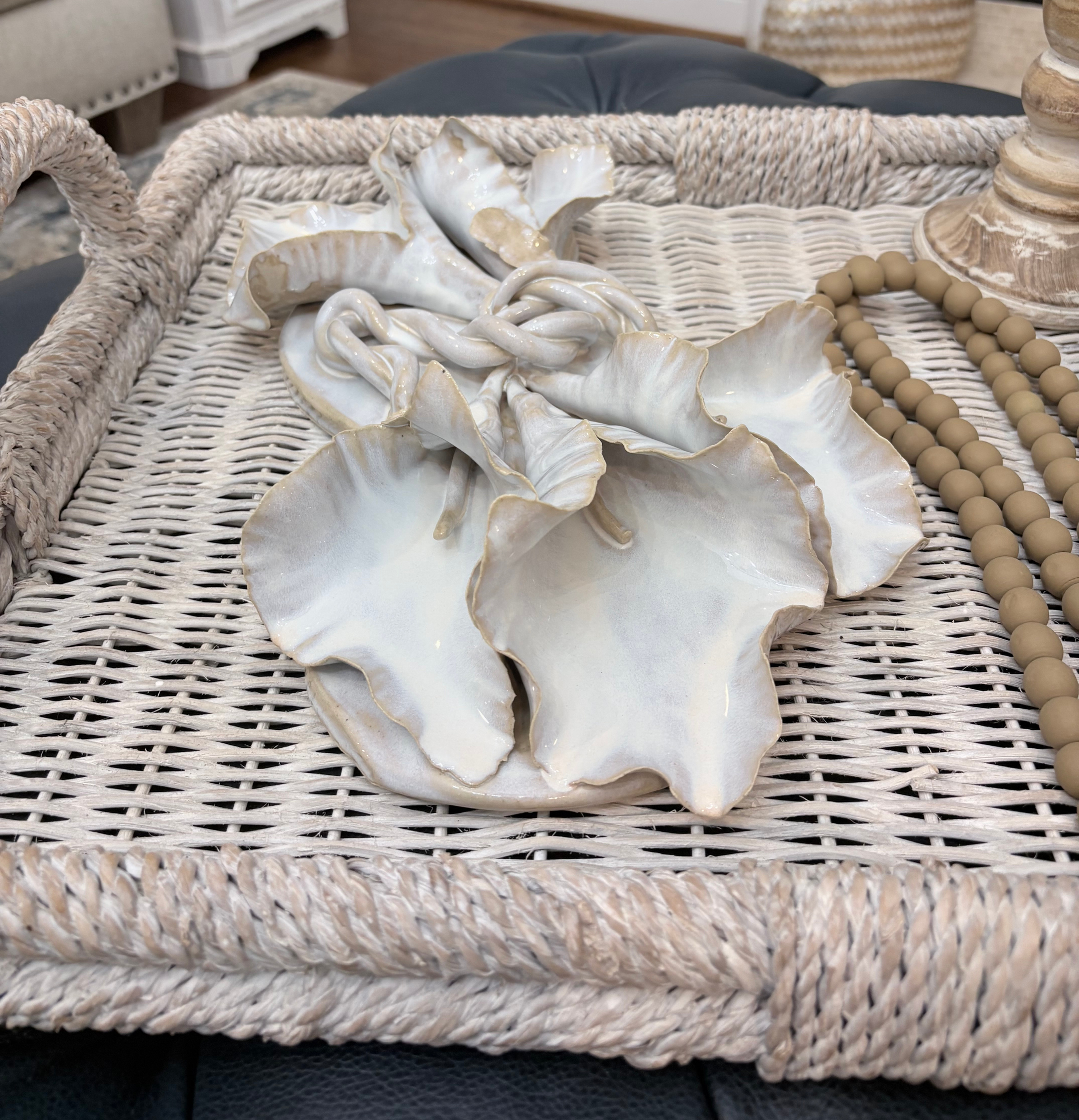 Wicker tray with white ceramic flower and tan bead garland on a table in a cozy neutral living room.