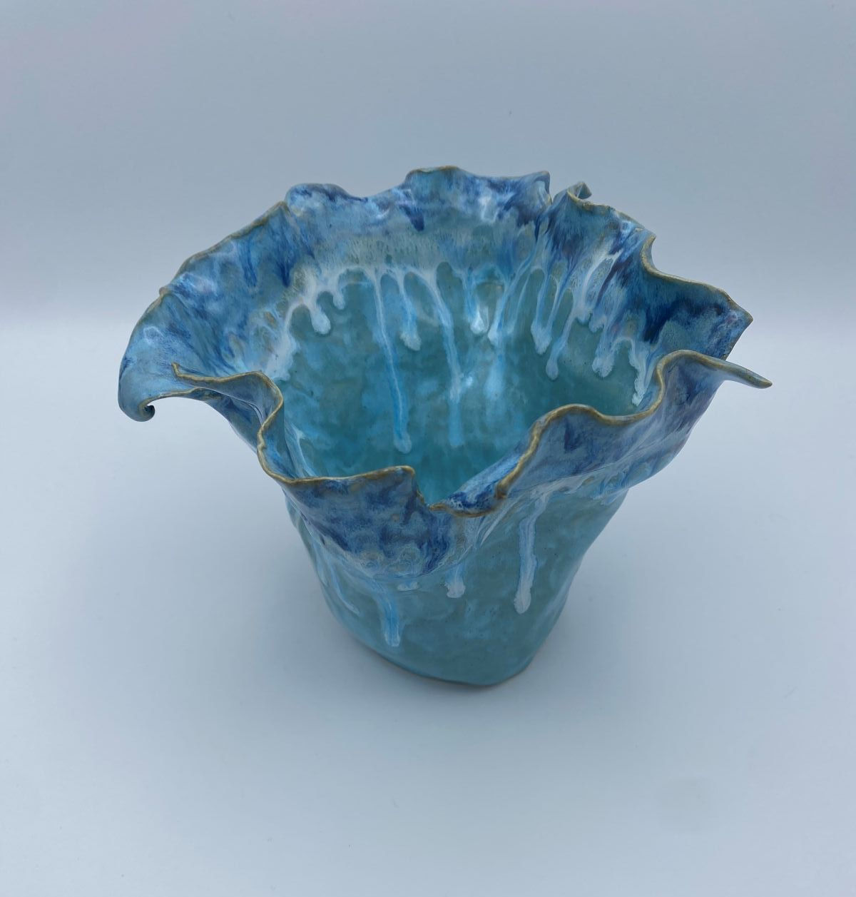 Blue ceramic vase with wavy, ruffled edges and white drip pattern, set against a plain background. The color evokes a serene,
