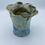 Thumbnail: Ceramic vase with wavy rim, glazed in earthy tones with blue drips. Set on a plain white background. Artistic and natural fee