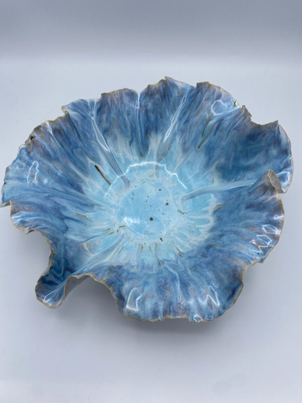 A blue, textured ceramic bowl with ruffled edges sits on a light background, resembling a blooming flower with a serene, artistic design.