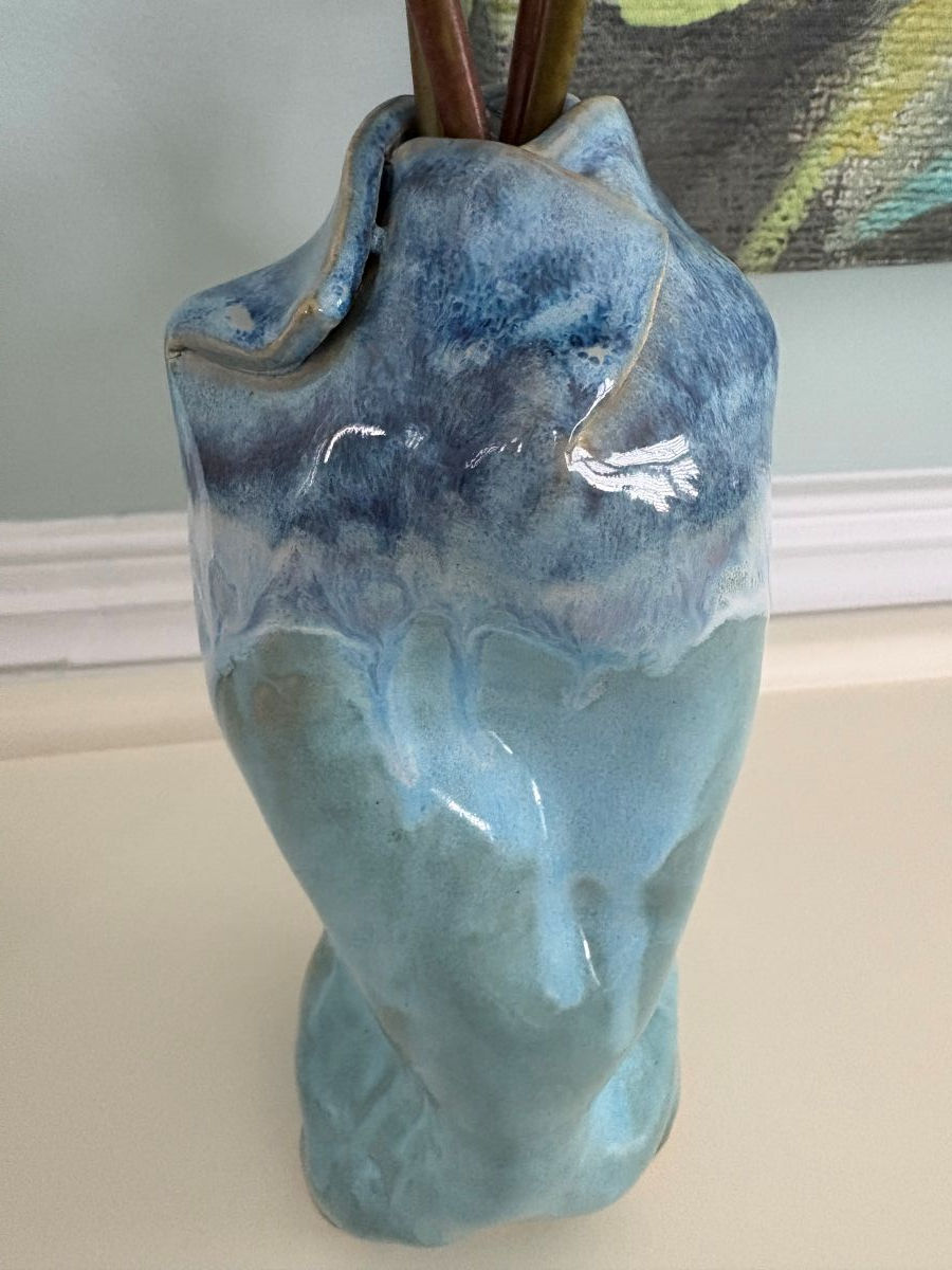 Thumbnail: Blue ceramic vase with a glossy finish and abstract shape sits on a light surface. Its top holds two plant stems