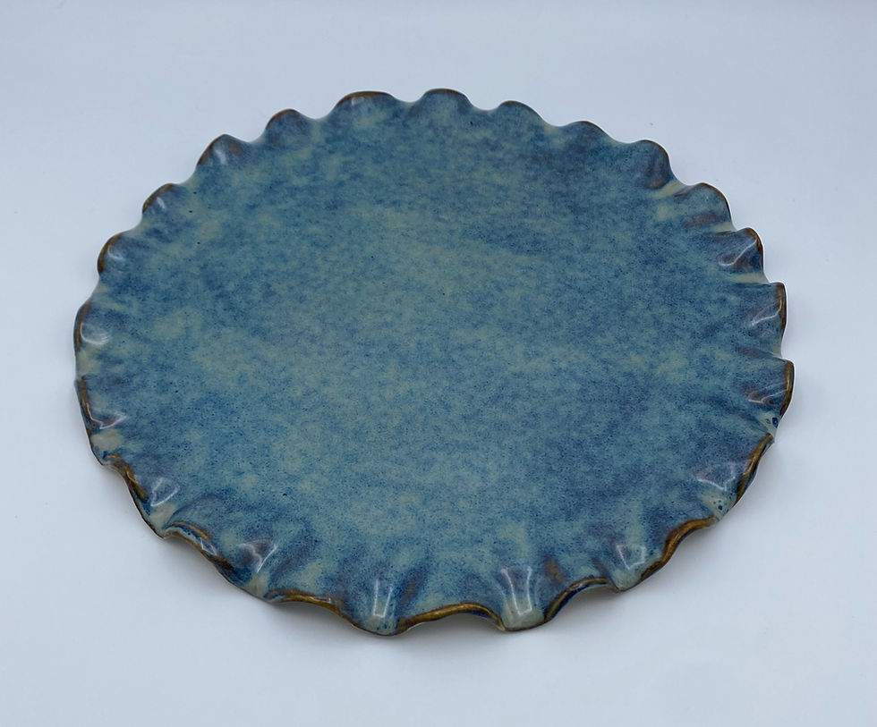 Blue ceramic plate with a ruffled edge on a white background. The plate has a speckled texture, creating a rustic and elegant appearance.