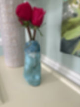 Two red roses in a blue ceramic vase with white drips, set on a light surface. A detailed white decorative object
