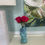 Thumbnail: Blue vase with pink roses on a beige surface, next to a white textured lamp and abstract painting. Calm setting