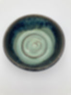 Blue-green ceramic bowl with a spiral pattern inside, set against a plain white background. The glaze is glossy and textured.