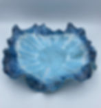 Blue ceramic bowl with ruffled edges and white patterned detail, set against a plain, light gray background.