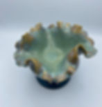 Green ceramic bowl with ruffled edges and brown accents on a white background. Smooth and glossy texture.