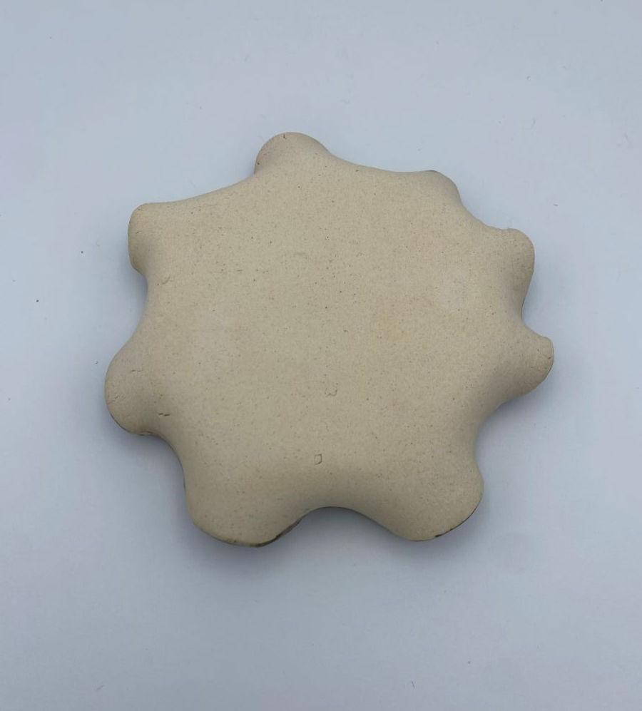 Thumbnail: Back of a handheld ceramic garlic grater looking like a star-shaped clay object on a plain gray background