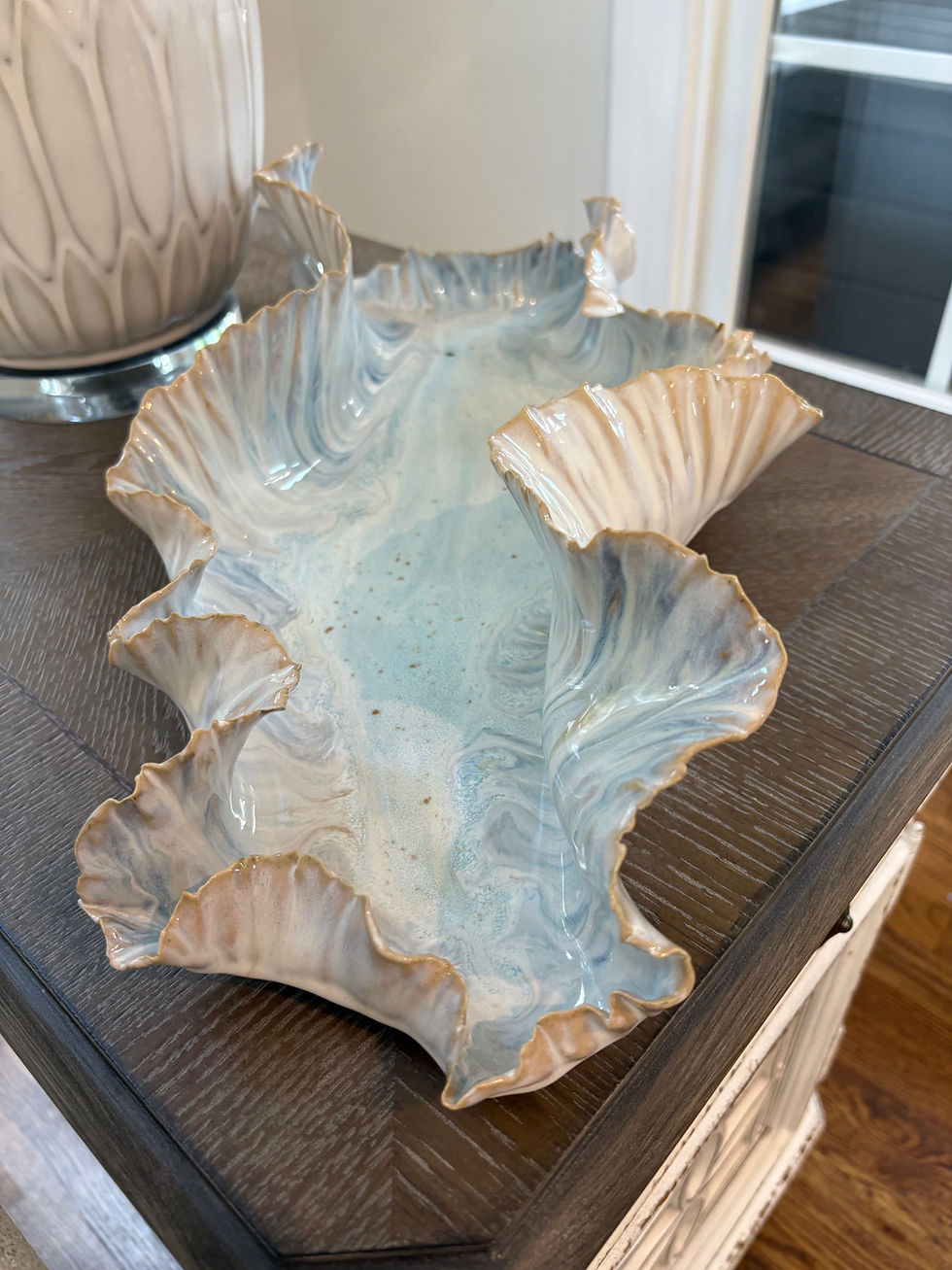 Ceramic ruffled bowl with blue and beige tones on a wooden table, next to a textured vase. Bright, elegant indoor setting.