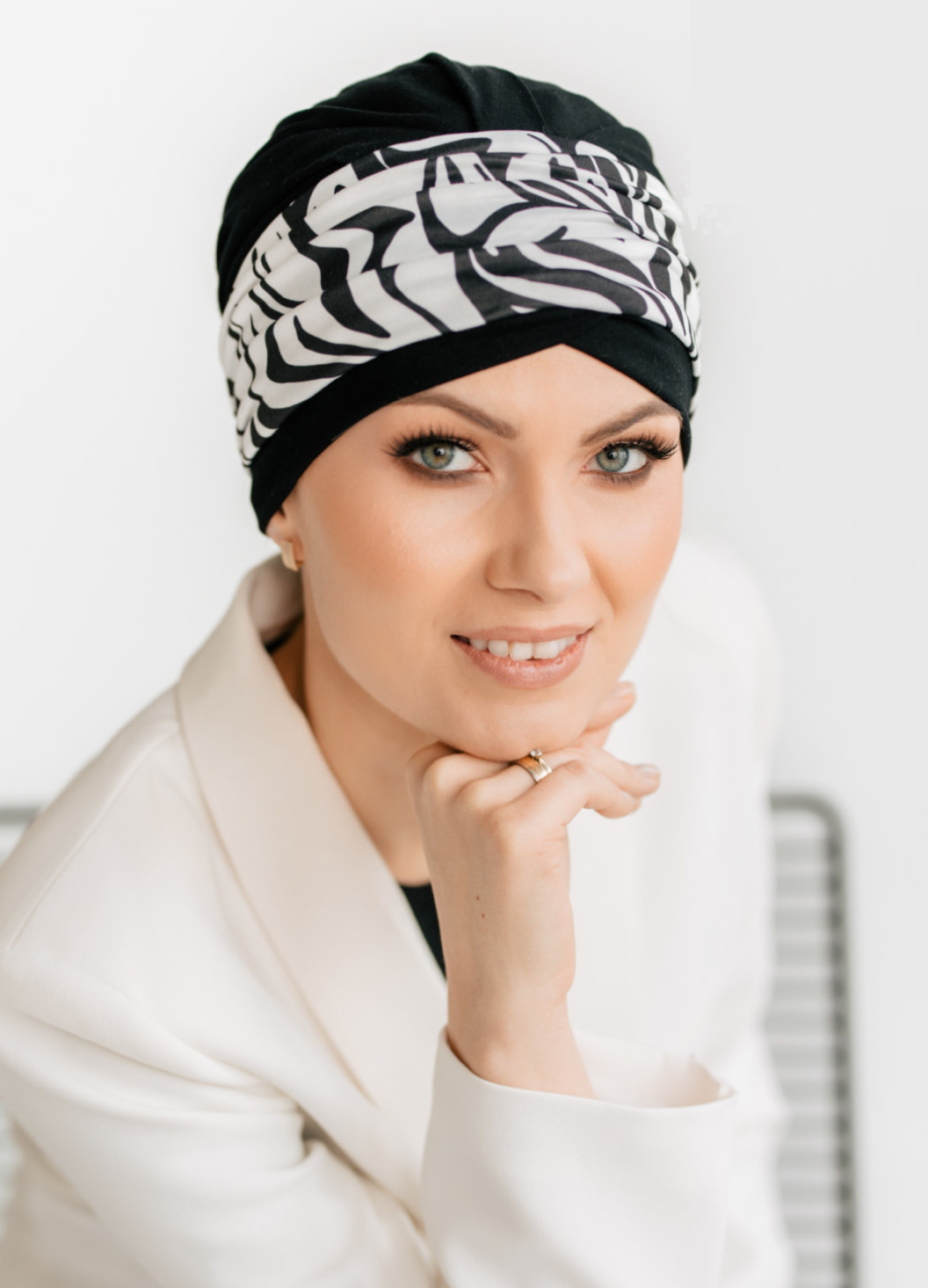 A woman wearing a black chemo hat featuring a black and white animal print headband
