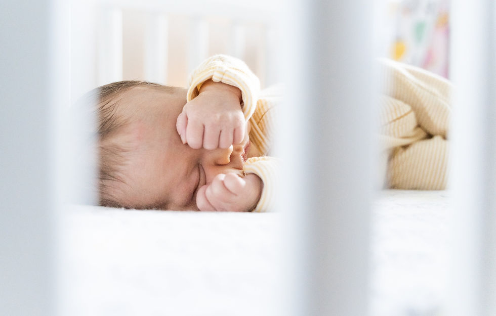 A baby sleeping in a crib rubbing his eyes