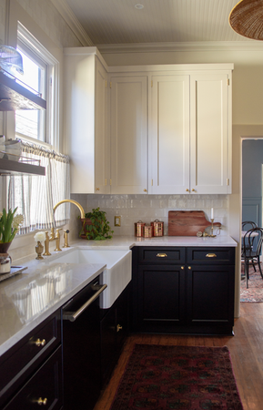 A kitchen in a Victorian home with white upper cabinets, black lower cabinets, white countertops, and brass accents and hardware.