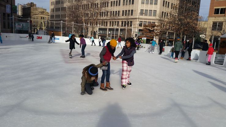 Black girl falling on ice on the ice rink in Minnesota. Her friends help her up.