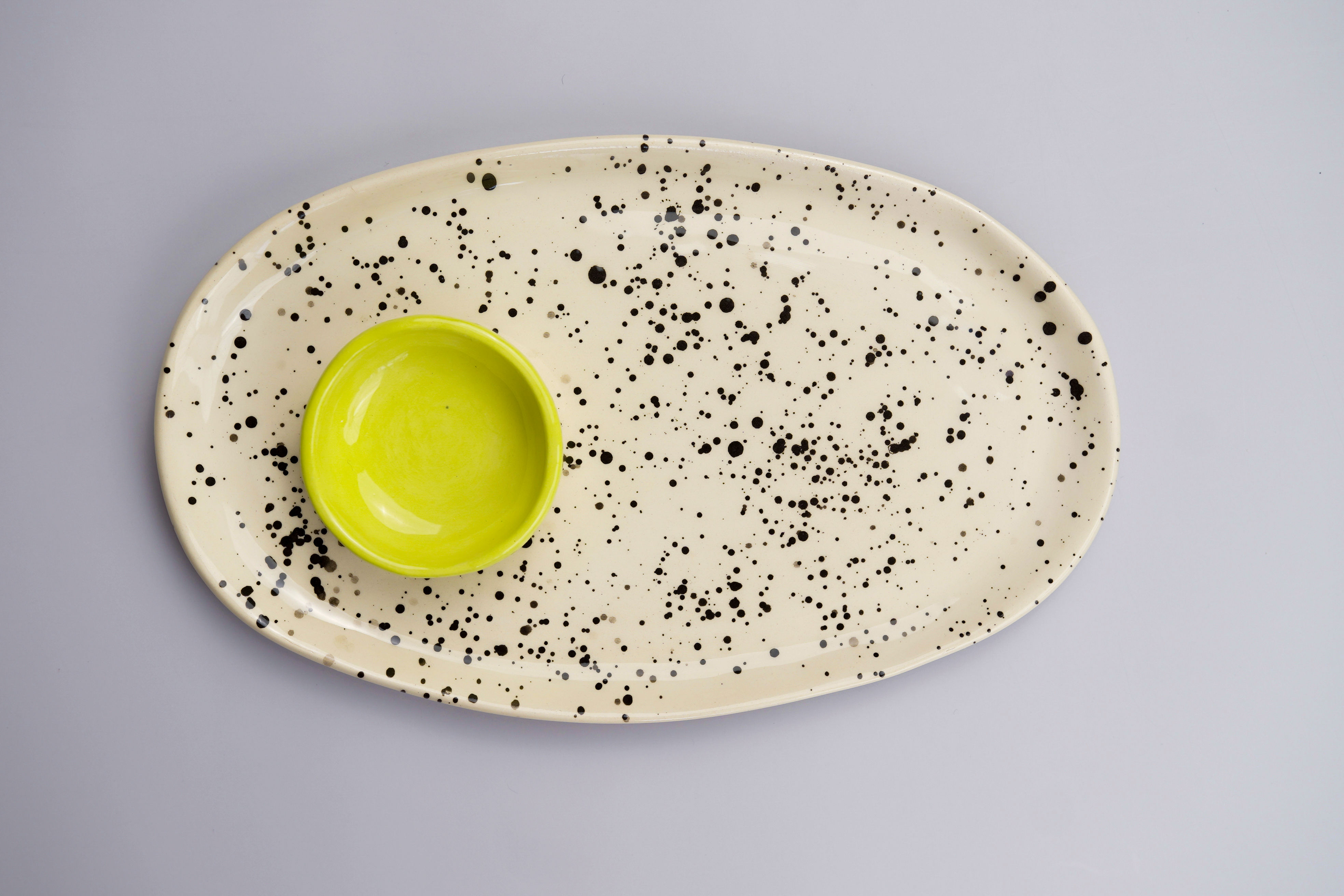 Plato ovalado beige con motas negras y cuenco amarillo sobre fondo gris.