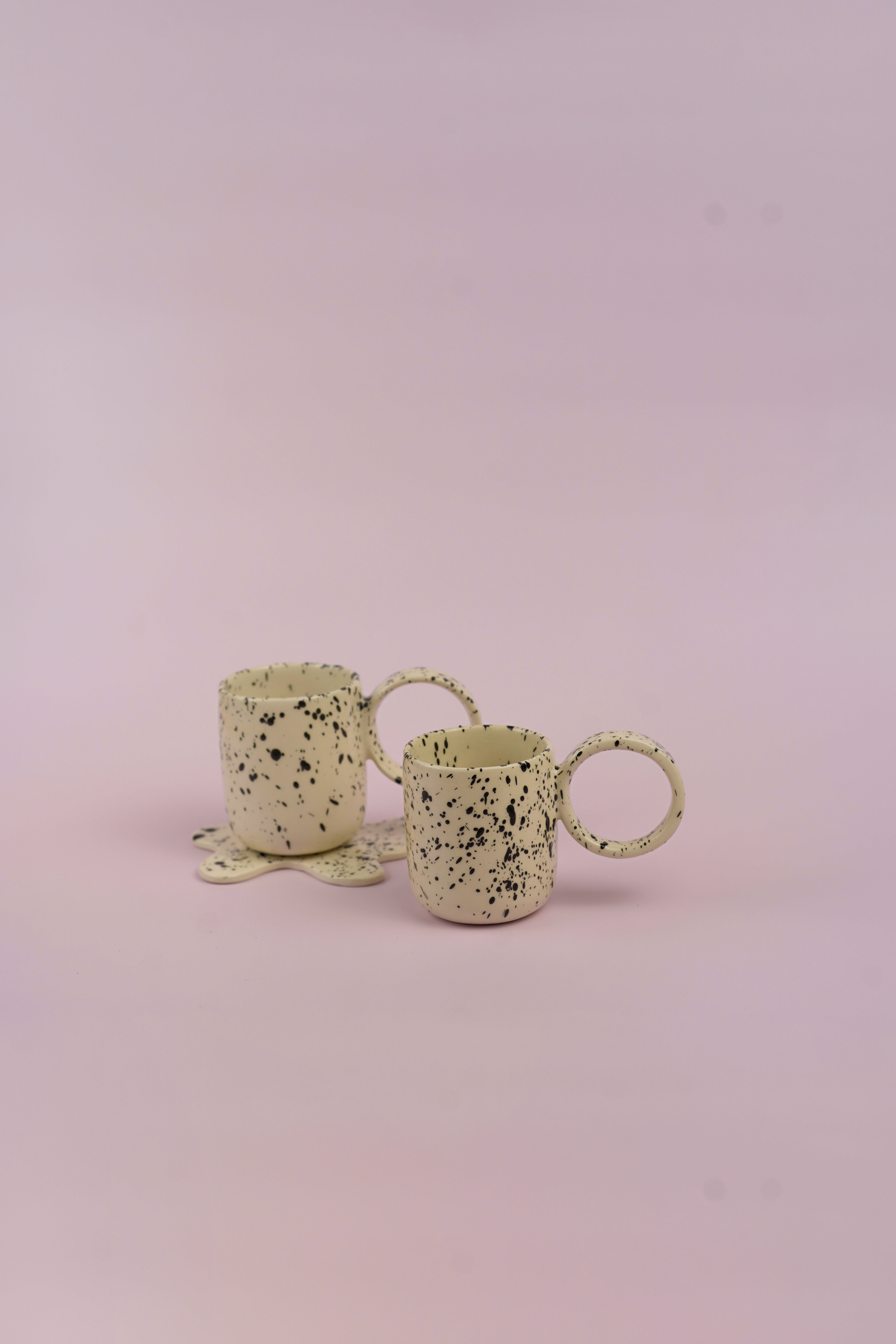 Dos tazas blancas con motas negras, sobre fondo rosa pastel. Ohdella!