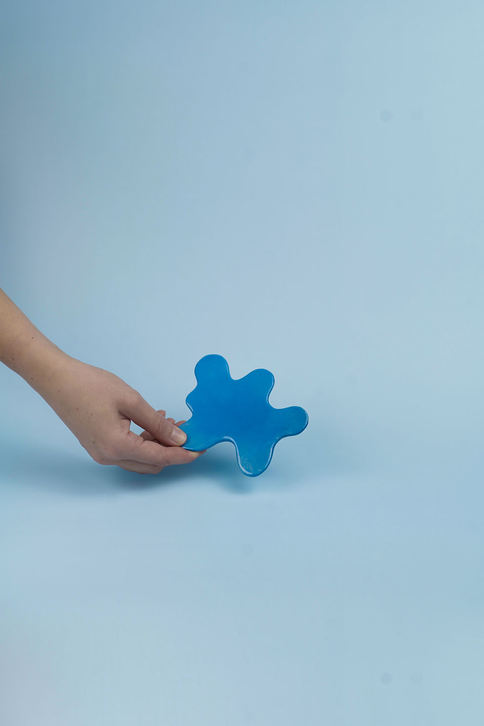 Mano sosteniendo un posavasos en forma de mancha azul sobre fondo celeste.
