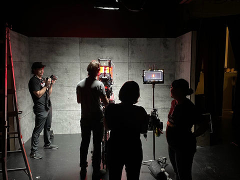 Film crew standing around a cinema camera inside a concrete chamber set.