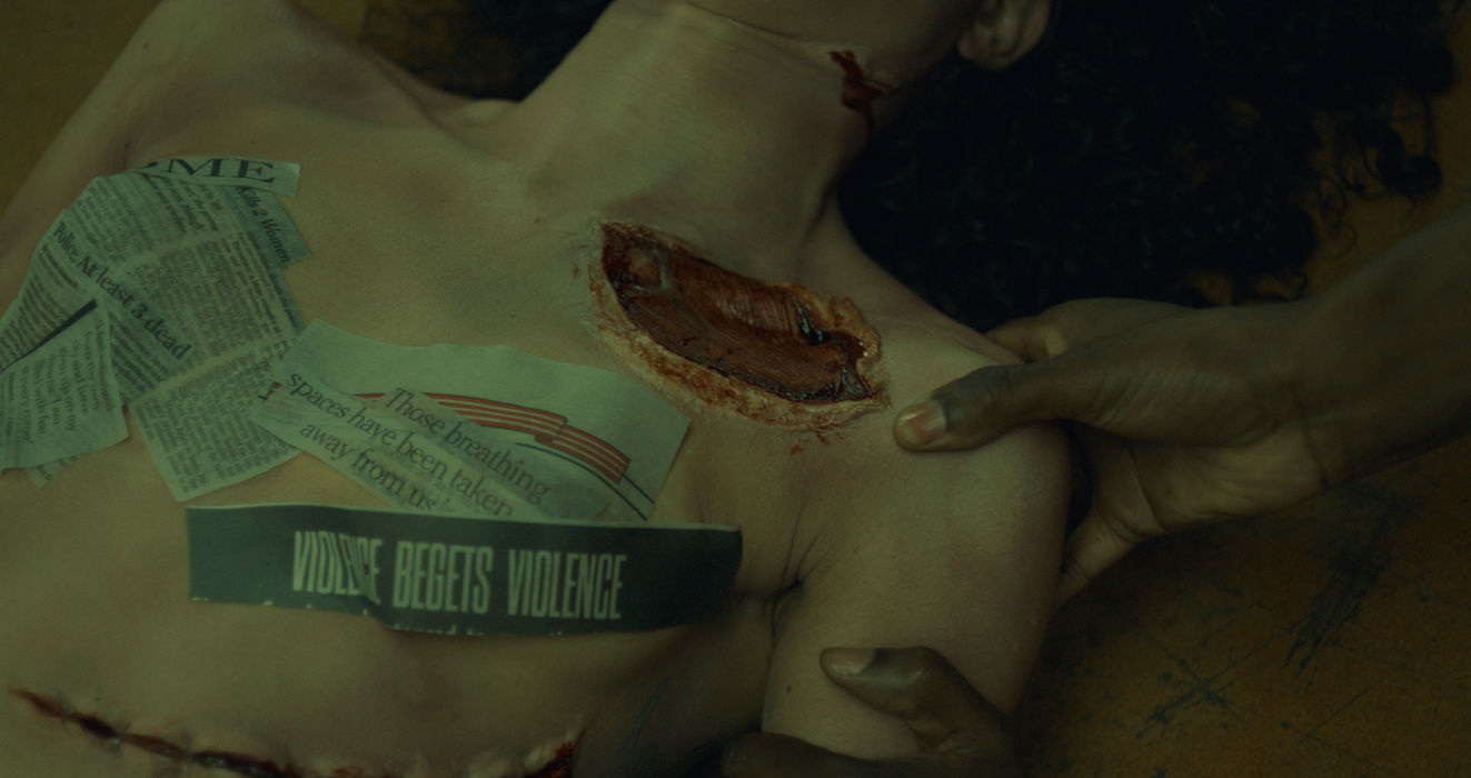 Close up of Carlita Tucker lying on table with newspaper clippings referencing violence.