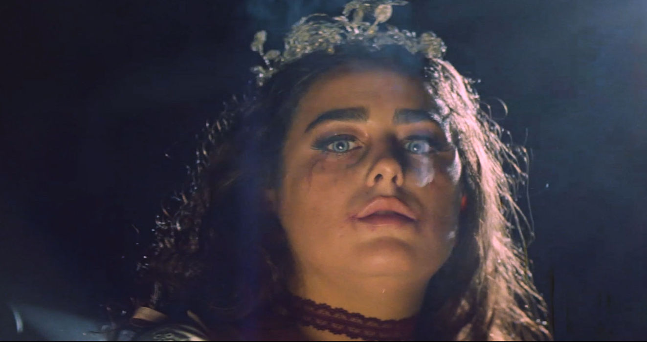 Woman with crown and emotional expression illuminated by dramatic stage lighting.
