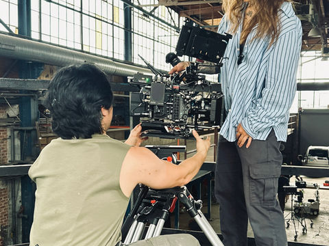 ARRI Alexa 35 cinema camera mounted on tripod positioned on an industrial catwalk inside a warehouse film location. Picture shows Gaffer Andy Cat and 1st AC Eva June with the camera.