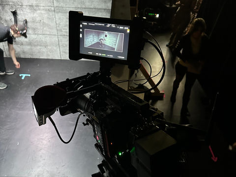 Cinema camera overlooking a concrete chamber set with actors preparing a scene.