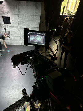 Cinema camera overlooking a concrete chamber set with actors preparing a scene.