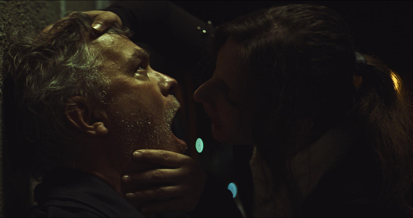 Woman gripping a man’s face against a wall during a violent moment.