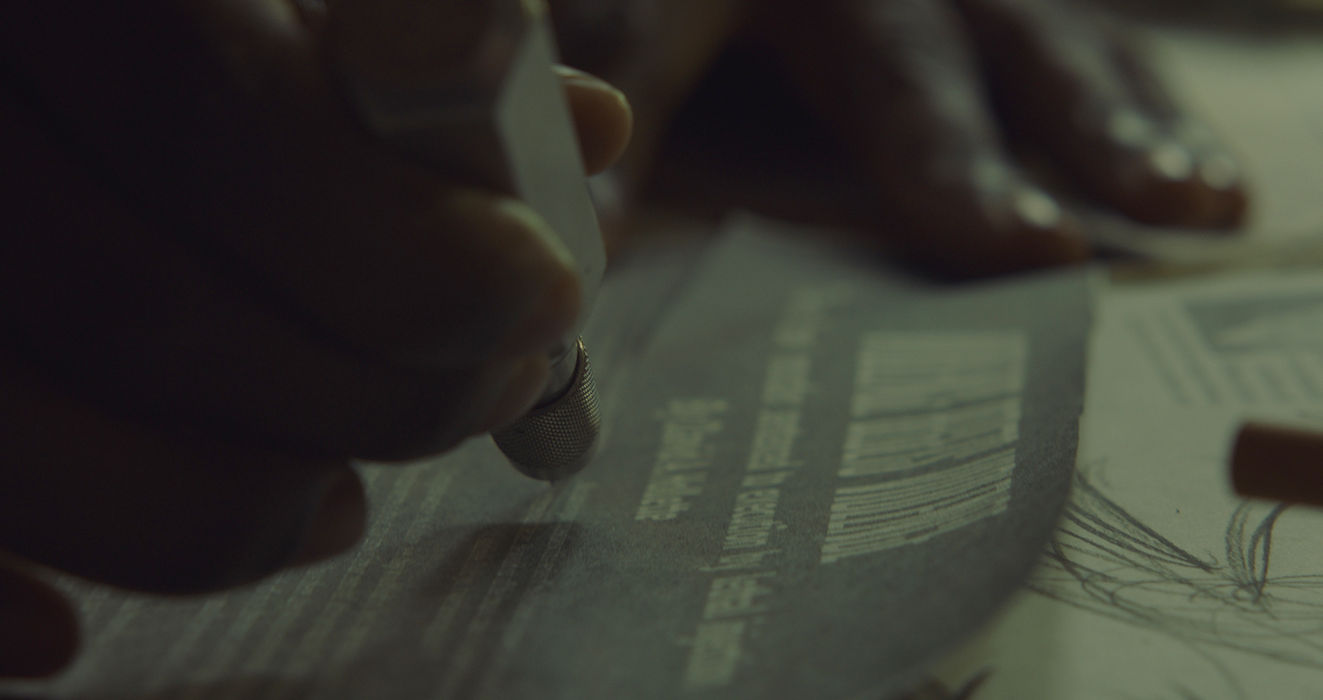 Hand using drafting tool and pencil to draw curved lines on a design sheet.