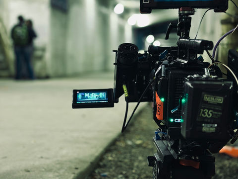 Cinema camera on tripod inside a tunnel filming actors in the distance.
