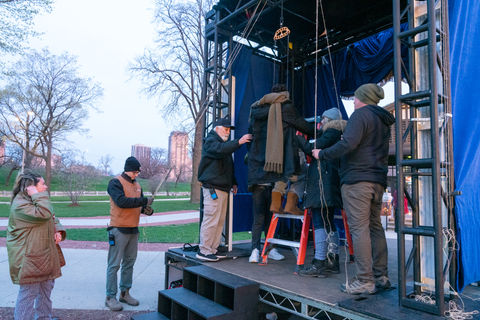 Crew adjusting ropes and rigging on puppet stage structure.