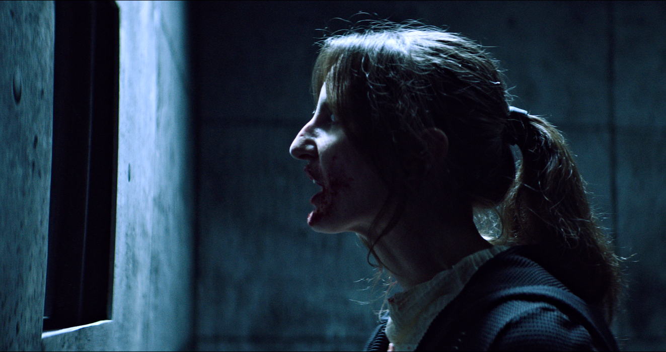 Woman yelling toward a small opening in a concrete wall.