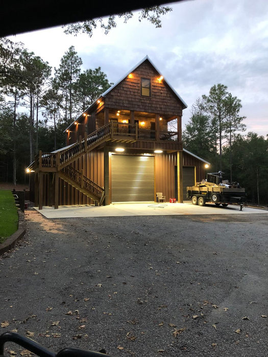Custom barn-style building illuminated at night with exterior lighting and roll-up doors