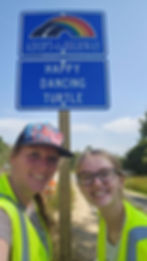 Two women in reflective vests by an adopt-a-highway sign.