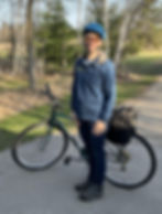 A woman dressed in blue standing next to a bike with trees in the background.
