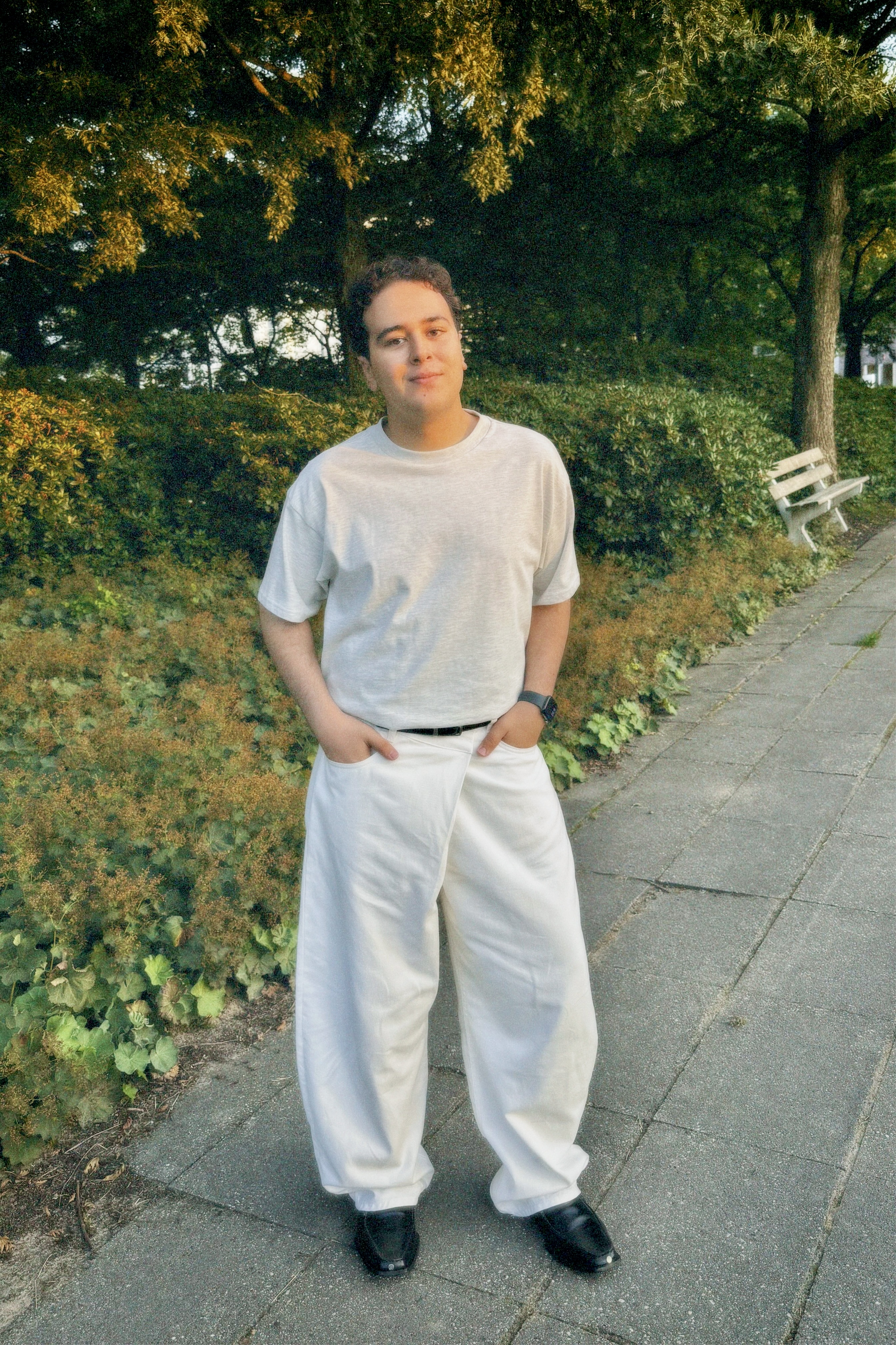 Modeportret van fotograaf en maker Yousri Adam in witte kleding in een park tijdens golden hour, met natuurlijke kleuren en r