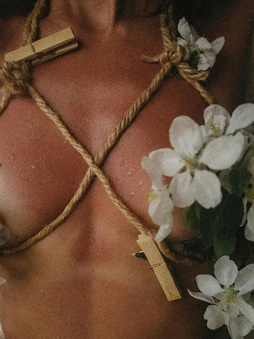 A person torso with rope crossing the chest and small flowers placed alongside. 