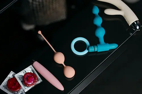 Sexual wellness items on a dark surface, including condoms, a vibrator, and silicone toys. 