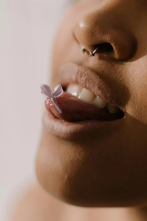Close-up of a person lips with a small flower resting on the tongue. 