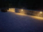 Illuminated stone retaining wall on a paved patio at night.