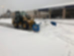 Wheel loader plowing snow in a Lowe's parking lot.